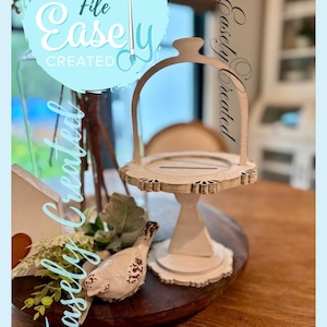 May include: A light-colored, wooden serving tray with a handle, featuring a decorative, scalloped edge. The tray is on a wooden base, with a small bird figurine and greenery nearby. The text "Digital Cut File Easely Created" is visible.