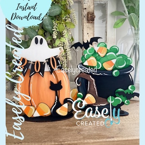 May include: Two Halloween-themed wooden decorations. The first is a pumpkin with a ghost and a black cat. The second is a cauldron with a witch's hat and bats. Both decorations have candy corn and green accents.