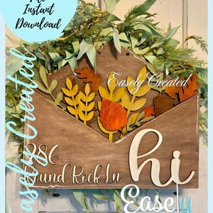 May include: A wooden sign shaped like an envelope with the words "Hi" and "286 Round Rock Ln" in a cursive font. The envelope is decorated with fall-themed leaves and branches. The sign is labeled "Easly Created".
