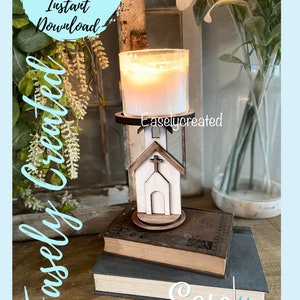 May include: A white wooden church-shaped candle holder with a cross on top. The candle holder is on a stack of books with the text "Easley Created" on the bottom book. A lit candle is in the holder.