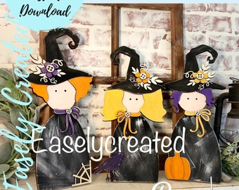 May include: Three black witch figures with orange, yellow, and purple hair, wearing black hats with floral accents. The figures are standing on a wooden shelf with a brick background. The text "Easlycreated" is visible in the image.