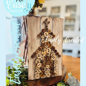 May include: Wooden house-shaped art piece made of various sized brown buttons. The house is mounted on a distressed, light-colored wooden board. The words "Easely Created" and "Digital Cut File" are visible in the image.