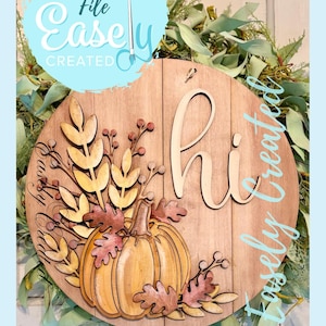 May include: Wooden round sign featuring a pumpkin and autumn leaves. The sign has the word "hi" in the centre and the text "Digital Cut File Easely Created" in light blue. The sign is surrounded by green foliage.