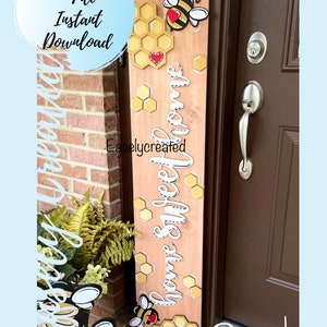 May include: Wooden sign with a light brown background, featuring a honeycomb design, bees, and the words "Home Sweet Home" in white script. The sign is decorated with yellow and red accents.