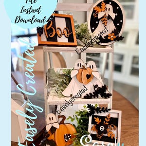 May include: A tiered shelf display featuring various Halloween-themed wooden cutouts. The top shelf has a round sign with a ghost and the text "Easlycreated". The middle shelf has two ghosts holding a pumpkin and the text "Easlycreated". The bottom shelf has a ghost holding a pumpkin, a square sign with black and white stripes and the text "Easly CREATED".