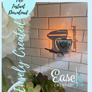 May include: A white and gray stand-alone night light shaped like a kitchen mixer with a bowl and spoon. The night light is plugged into an electrical outlet on a white tiled wall. The text "Easley Created" is visible in the image.