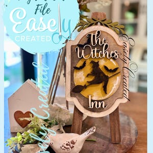 Puede incluir: Un letrero de madera con el texto "The Witches Inn" y una silueta de una bruja volando en una escoba frente a una luna amarilla. El letrero está sobre un pequeño caballete de madera. También se ven las palabras "Digital Cut File Easely Created".