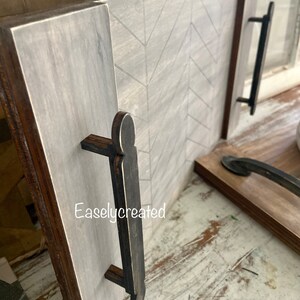 May include: A wooden serving tray with a chevron pattern and two black wooden handles. The tray is painted in a light gray color with a distressed finish. The text "Easlycreated" is visible on the tray.