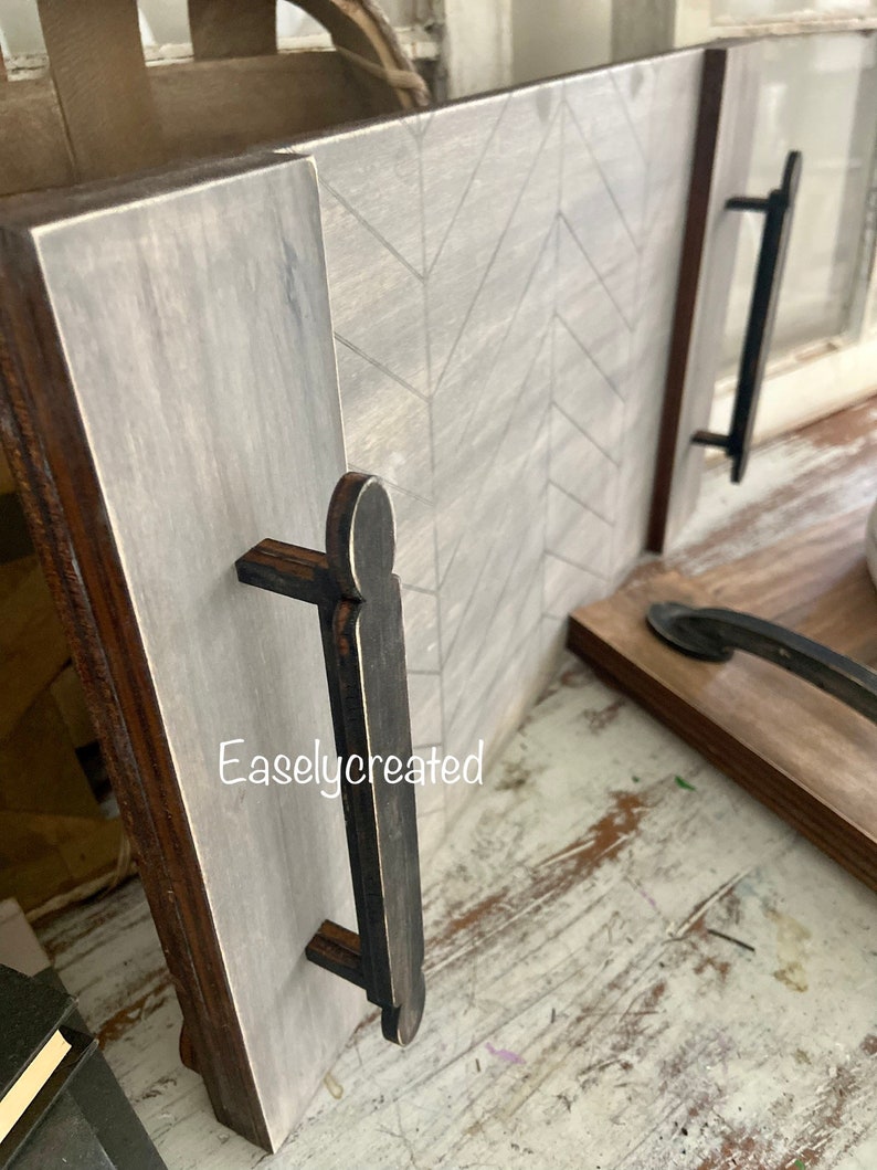 May include: A wooden serving tray with a chevron pattern and two black wooden handles. The tray is painted in a light gray color with a distressed finish. The text "Easlycreated" is visible on the tray.