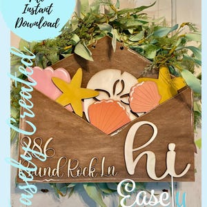 May include: A wooden sign shaped like an envelope with the words "Hi" and "286 Round Rock Ln" written on it. The envelope is open and has various cut-out shapes inside, including a starfish, seashells, and a sand dollar. The sign is decorated with a green leafy garland and the words "Easley Created" are at the bottom.