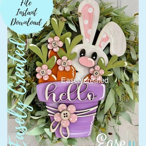 Può includere: Un vaso di fiori viola con un coniglietto bianco che spunta dalla parte superiore. Il vaso ha la scritta "hello" e  è decorato con fiori rosa e un fiocco.