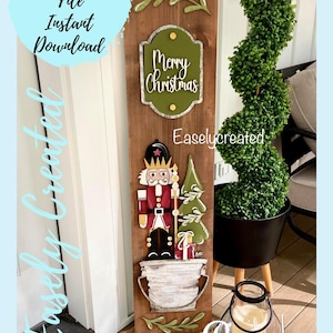 Puede incluir: Un letrero de madera con un cascanueces, un árbol de Navidad y un letrero que dice "Feliz Navidad". El letrero está decorado con vegetación y se apoya en una puerta blanca. El letrero está sobre una alfombra de color marrón y blanco con un patrón.