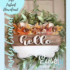 Puede incluir: Un letrero de madera blanco con un borde festoneado y la palabra "hello" escrita en cursiva en una tabla de madera marrón. El letrero está decorado con hojas de otoño y bellotas y rodeado de una corona de hojas verdes. El texto "Easlycreated" es visible en el letrero.