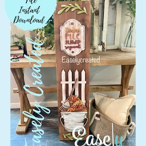 May include: A wooden sign with a fall theme. The sign says "Rake Pile Jump Repeat" and has a picture of a bucket with leaves and a rake. The sign is on a wooden table with a basket and a pillow.