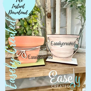 Könnte beinhalten: Zwei hölzerne Pflanzgefäße, eines mit abgerundeter Oberseite und das andere mit rechteckiger Oberseite. Beide Pflanzgefäße sind in einem hellen Rosa gestrichen und tragen den Text "Easlycreated". Die Pflanzgefäße stehen auf einem Holztisch.