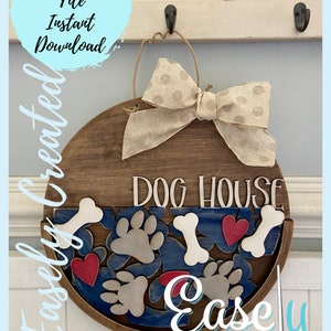 May include: A round wooden sign with the text "Dog House" in white lettering. The sign is decorated with a beige bow, paw prints, bones, and red hearts. The sign is hanging on a white hook.