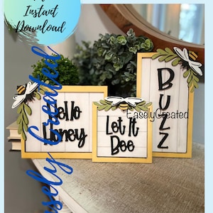 May include: Three wooden signs with a yellow frame and white background. The signs feature black lettering with bee and leaf accents. The signs read "Hello Honey", "Let It Bee", and "Buzz".
