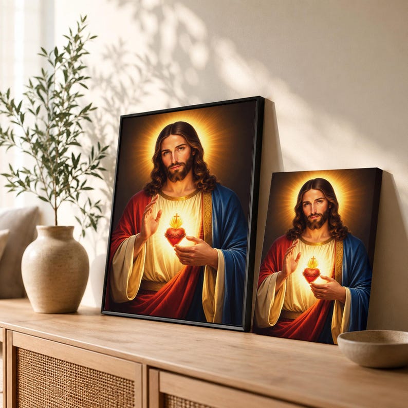 Two sizes of the Sacred Heart of Jesus canvas prints displayed side-by-side on a wooden credenza. The beautiful Christian artwork showcases rich red and blue robes with glowing golden light textures. Perfect size guide for customers looking to choose religious wall art for their home altar, bedroom, or parish.