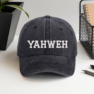 Op de afbeelding: Een zwarte baseballcap met het woord "YAHWEH" in wit geborduurd. De cap heeft een gebogen klep en een versleten, vintage uitstraling. De hoed is gemaakt van een zachte, duurzame stof.