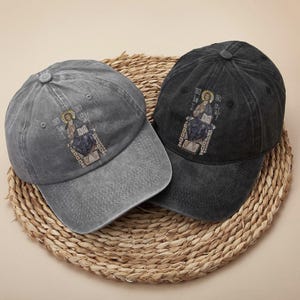 Set of two vintage-inspired washed cotton caps in gray and black, each adorned with a detailed embroidery of Christ sitting on a throne. The design exudes a powerful faith-based message, perfect for expressing religious beliefs. These unisex hats offer a comfortable and adjustable fit, ideal for everyday wear, casual gatherings, or church activities. A thoughtful gift for believers or anyone seeking stylish, meaningful accessories.