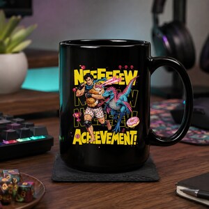 May include: A black ceramic mug featuring a graphic illustration of a character holding a cat with laser eyes next to a blue dinosaur. The design includes the text "NEEEEEEW ACHIEVEMENT!" in bold yellow letters, along with small icons of a trophy, a donut, and skulls.