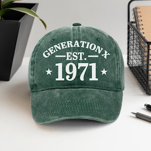 Könnte beinhalten: Grüne Baseballkappe mit weißem Text "GENERATION X EST. 1971". Die Kappe hat einen gebogenen Schirm und einen Knopf oben. Der Text ist zentriert, mit einem Stern auf jeder Seite des Jahres. Ein lässiges Accessoire.