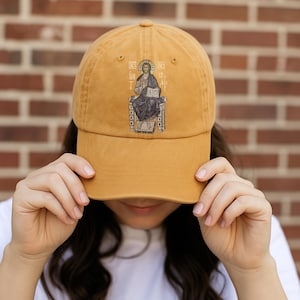 Custom ginger-colored cap featuring an embroidered icon of Christ the King. The person is holding the hat against a brick wall background, showcasing the religious design. This hat is perfect for faith-based fashion, personalized religious gifts, and spiritual wear. A unique accessory for those looking to add a meaningful, Christian-themed item to their wardrobe.