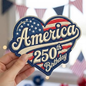 May include: Embroidered patch in a heart shape, featuring the American flag design. The patch has the word "America" in a cream-colored script, with "250th Birthday" below. The patch is blue, red, and cream-colored.