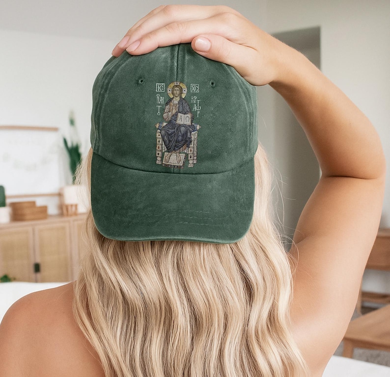 A woman wearing a green washed cotton cap featuring an intricate embroidery of Christ seated on a throne. The cap symbolizes faith, offering a stylish and spiritual accessory for casual outings. With an adjustable strap, this hat ensures a comfortable fit and is perfect for expressing your Christian beliefs or gifting to loved ones. Ideal for church, daily wear, or as a meaningful token for those who embrace their faith.