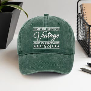 Op de afbeelding: Een groene baseballcap in vintage-stijl met de tekst "LIMITED EDITION Vintage AGED TO PERFECTION 1924" in het wit. De cap heeft een gebogen klep en een distressed look, wat een retro esthetiek suggereert. De hoed is gemaakt van zacht materiaal.
