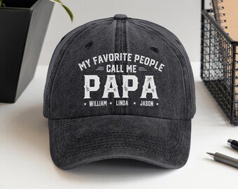May include: A dark gray baseball cap with the text "MY FAVORITE PEOPLE CALL ME PAPA" in white. Below the word "PAPA" are the names "WILLIAM", "LINDA", and "JASON". The cap has a curved brim and a button on top.