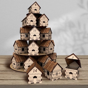 May include: A wooden advent calendar shaped like a Christmas tree, featuring small house-shaped boxes with numbers 1-24. Each house has a decorative design and a small door. One house is open, revealing the interior.