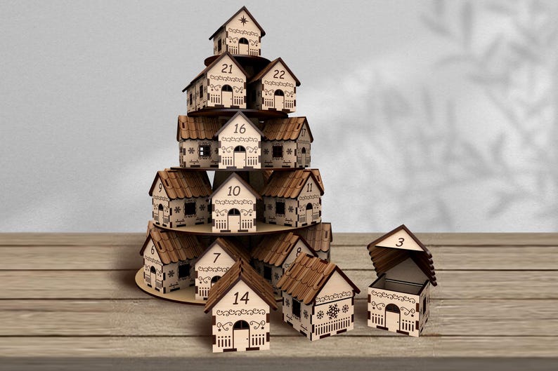 May include: A wooden advent calendar shaped like a Christmas tree, featuring small house-shaped boxes with numbers 1-24. Each house has a decorative design and a small door. One house is open, revealing the interior.