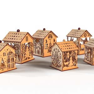 Peut inclure: Plusieurs photophores en forme de maison en bois d&eacute;coup&eacute; au laser. Chaque maison pr&eacute;sente des motifs d&eacute;coup&eacute;s de stars, d'arbres et d'&eacute;l&eacute;ments festifs. Les maisons sont en bois brun clair et sont con&ccedil;ues pour contenir des bougies.