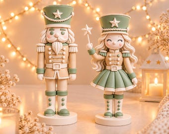 Könnte beinhalten: Zwei Nussknacker-Figuren in Salbeigrün und Creme. Die linke Figur ist ein Soldat mit Schnurrbart und Uniform. Die rechte Figur hat langes, welliges Haar und hält einen Zauberstab mit Stern. Beide stehen auf runden Sockeln.