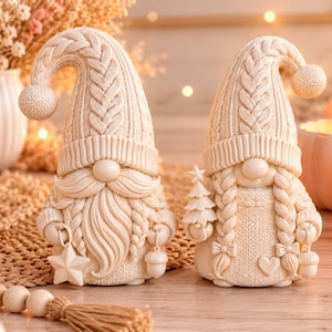 Könnte beinhalten: Zwei cremefarbene Zwergenfiguren mit strukturierten, gestrickt wirkenden Mützen und Kleidung. Der linke Zwerg hat einen langen Bart und hält einen Stern und eine Eichel. Der rechte Zwerg hat geflochtene Haare, hält einen Baum und hat kleine Schleifen.