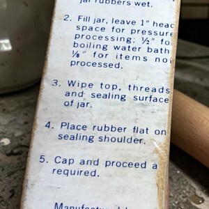 May include: Close-up of a vintage Ball Corporation box with canning instructions. The box is off-white with blue text detailing the steps for canning, including washing jars, filling, and sealing. The box is slightly worn.