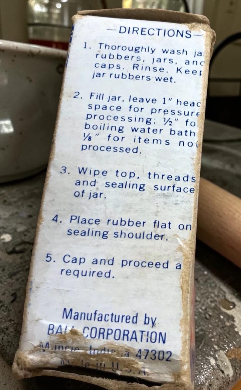 May include: Close-up of a vintage Ball Corporation box with canning instructions. The box is off-white with blue text detailing the steps for canning, including washing jars, filling, and sealing. The box is slightly worn.