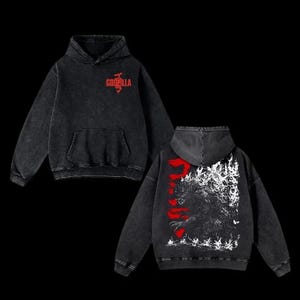 Può includere: Due felpe con cappuccio nere con tasca frontale e cappuccio. Una ha la scritta "GODZILLA" in rosso sul davanti. L'altra ha una grafica di Godzilla sul retro con testo giapponese e fiamme bianche e rosse.