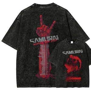 Pode incluir: Duas camisetas pretas com lavagem ácida e gráficos vermelhos. Uma camiseta apresenta um gesto de mão e a palavra "SAMURAI" com "REUNION TOUR EVER" e uma lista de cidades. A outra tem um gráfico vermelho e as palavras "SAMURAI" e "REUNION TOUR 2023".
