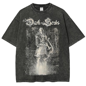 Op de afbeelding: Donkergrijs T-shirt met een verweerde afbeelding van een ridder met zwaard en schild. De tekst "Dark Souls" staat in een sierlijk lettertype boven de ridder gedrukt. Het shirt heeft een vintage, gewassen uitstraling.