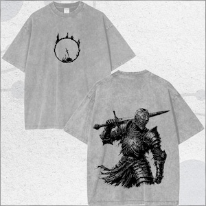 May include: A grey acid-wash t-shirt featuring a small black graphic of a sword inside a flaming circle on the front chest and a large black detailed illustration of a knight in full plate armour holding a sword on the back.