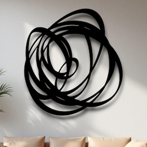 May include: A large, abstract black metal wall art piece with a swirling, looped design. The artwork is mounted on a white wall above a beige sofa with matching pillows. A potted plant sits to the left.