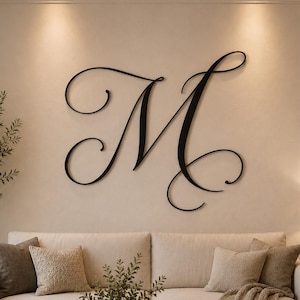 Può includere: Una grande lettera M decorativa da parete in colore nero, realizzata in corsivo con eleganti curve e volute. La lettera è fissata su una parete di colore chiaro sopra un divano, fungendo da elemento centrale e distintivo dell'ambiente.