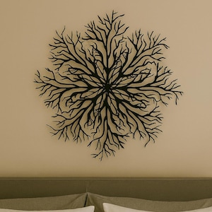 May include: Black metal wall art in a circular, branching design, resembling a stylized tree or coral. The artwork is mounted on a neutral-colored wall above a bed with gray bedding and white pillows.