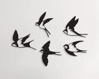 May include: Black and white swallow wall art. Six swallows are depicted in flight, with their wings spread. The swallows are mounted on a white wall. The image also shows a white staircase and a white vase with branches.