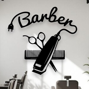 Może przedstawiać: Czarna naklejka ścienna z napisem Barber wykonanym kursywą, z wtyczką elektryczną na początku litery B, umieszczona nad grafiką przedstawiającą maszynkę do strzyżenia włosów, nożyczki i grzebień ułożone w kształt krzyża.