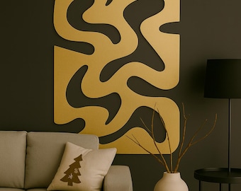 Könnte beinhalten: Ein großes, goldfarbenes Wandkunstwerk mit einem abstrakten, fließenden Design ist an einer dunklen Wand angebracht. Das Kunstwerk ist rechteckig mit ausgeschnittenen Formen. Ein beiges Sofa mit einem dekorativen Kissen und eine schwarze Lampe befinden sich im Vordergrund.