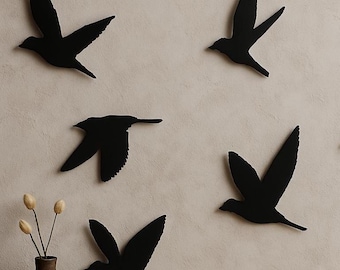 May include: A set of five black bird silhouettes arranged in a flying formation. Each bird is depicted in a different pose with wings spread or angled. The birds are flat, solid black shapes that contrast against the light-colored wall surface.