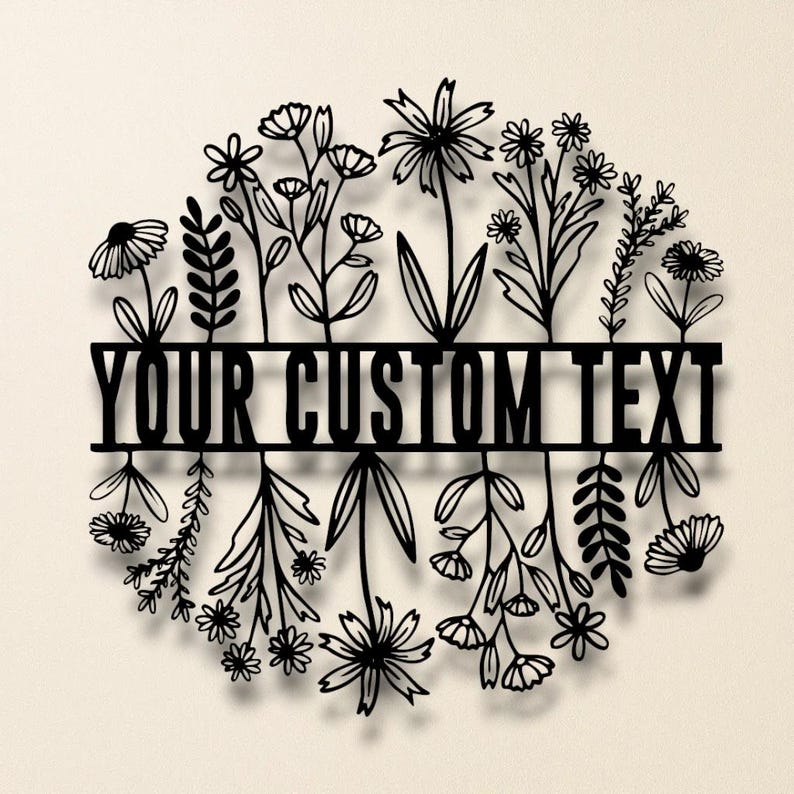 Puede incluir: Corona floral de metal negro con el texto "YOUR CUSTOM TEXT" en el centro. La corona presenta varias flores y follaje estilizados, creando un dise&ntilde;o decorativo. El fondo es de color beige claro s&oacute;lido.